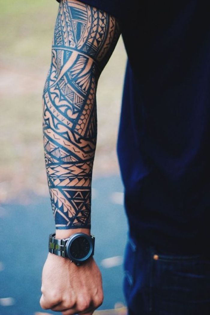 ein mann mit blauen hosen, uhr und einem großen schwarzen tattoo mit vielen schwarzen maori tattoo motiven