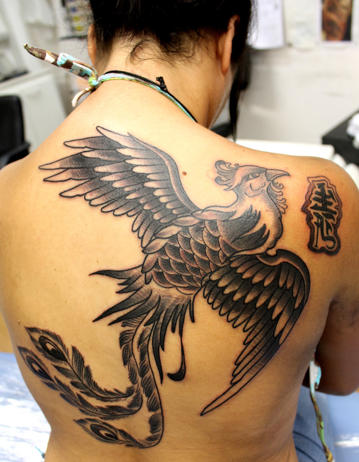 junge frau mit einer schwarzen tätowierung mit einem großen schwarzen fliegenden phönix mit zwei schwarzen flügeln mit schwarzen und weißen federn, phönix Tattoo Rücken Frau