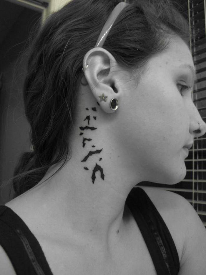 hunterm ohr tattoo - eine junge frau mit einem kleinen schwarzen tattoo hinter ihrem ohr - mit vielen schwarzen fliegenden fledermäusen 