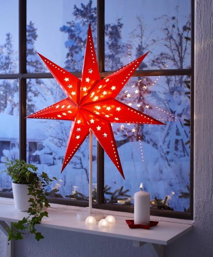 Stehlampe mit rotem Papier-Schirm in der Form eines Sterns, angezündete Kerze aus weißem Wachs, grünes Rankengewächs in einem weißen Blumentopf aus Keramik, Winterlandschaft mit viel Schnee