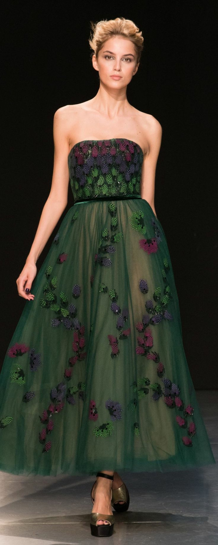 langes dunkelgrünes schulterfreies Kleid mit schmalem schwarzen Gürtel und vielen blauen, lila und grünen Applizierungen, kombiniert mit Plattformsandalen in Goldfarbe