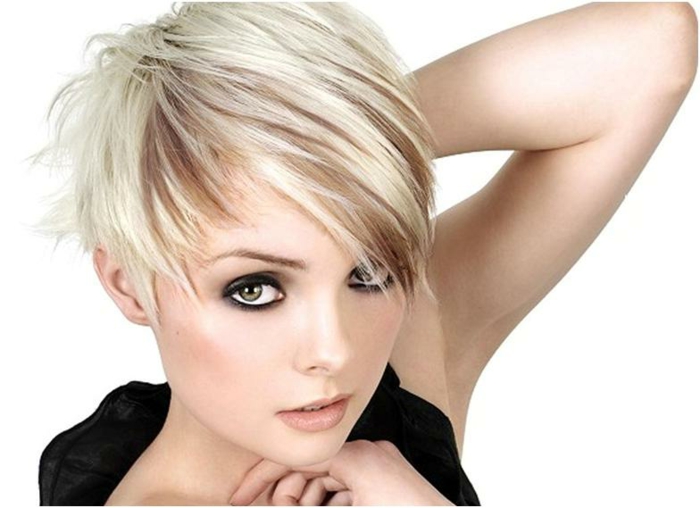 90s Look - strukturierter kurzer Haarschnitt mit Seitenpony, weißblonde Haare mit braunen Strähnen, dünn gezupften Augenbrauen, schwarzer Eyeliner und orangenfarbenes Rouge, große grüne Augen