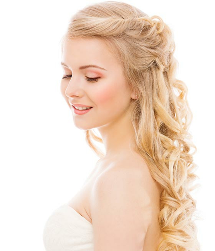 blondes lockiges Haar mit Twist, Frisur mit Seiten-Twist, rosa Schminke mit schwarzem Ezeliner, kleine weiße Zähne, weißes Kleid schulterfrei, Hochzeitskleid ohne Träger