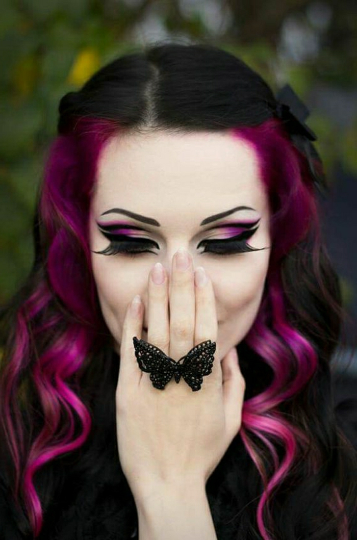 Gothik-Look - schwarzes Haar mit violetten Seitensträhnen mit großen Locken, starke violett-weiße Schminke - Lidschatten in zwei Farben, schwarzer Lidstrich und riesige künstliche Wimpern, Seitensträhnen gesteckt nach hiinten mit zwei schwarzen Haarklammern, schwarzer Ring in der Form eines Schmetterlings