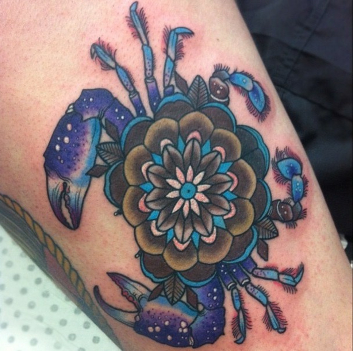 große Tätowierung des Sternzeichens Krebs mit einer Blume in der Mitte, blau-lila Sternzeichen-Tattoo mit einem kleinen Mandala, Krebstattoo mit Blumenmotiv