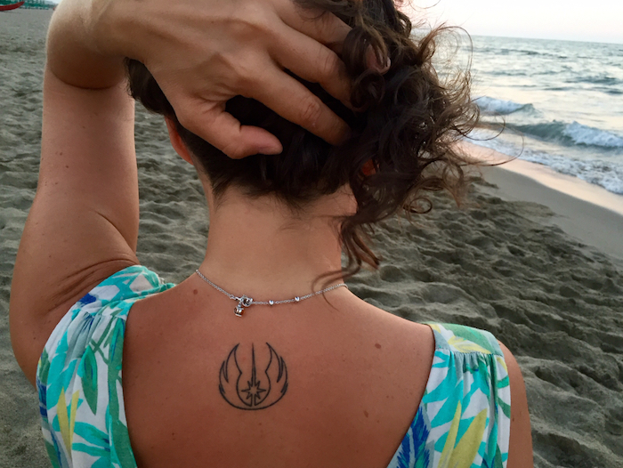 junge frau mit einem star wars tattoo mit einem kleinen star wars logo - meer und strand mit sand