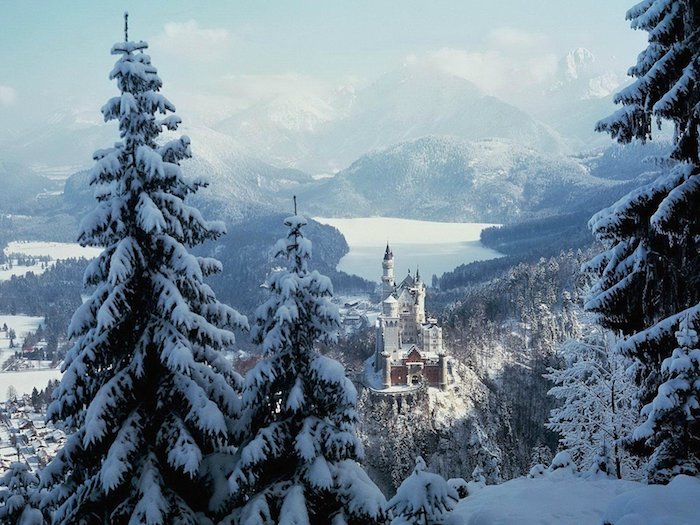 ein romantisches winterbild mit einem weißen schloss mit türmen und einem wald mit vielen bäumen - berge mit schnee - blauer himmel mit weißen wolken