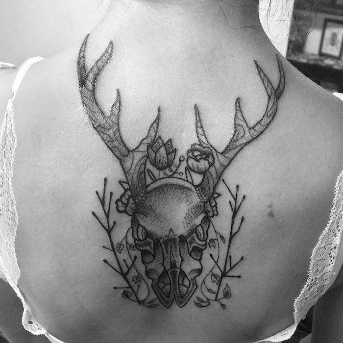 tattoo totenkopf - eine frau mit einem schwafrzen tattoo mit einem totenkopf eines hirsches mit großen hörnern und zwei kleinen blumen