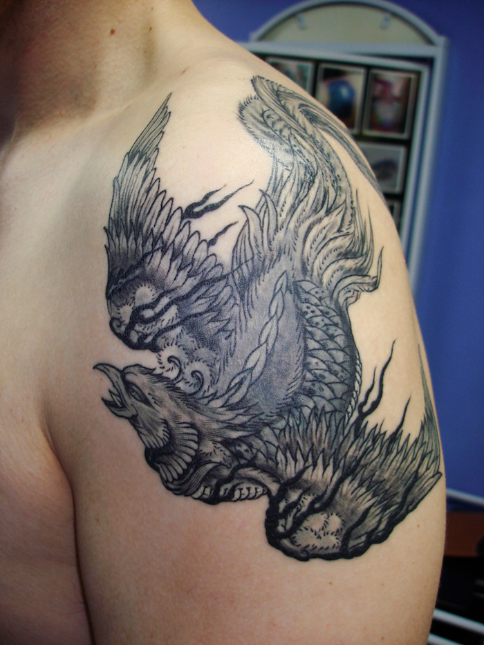 phönix Tattoo Schulter, ein mann mit einer hand mit einem schwarzen tattoo mit einem fliegenden schwarzen phönix mit weißen und schwarzen federn - männer tattooo mit phönix, 