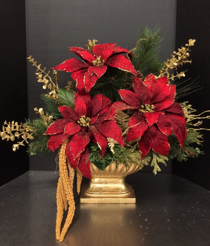 Adventsgestecke Ideen - drei Weihnachtssterne in einer goldenen Vase, mit grünen Zweigen dekoriert