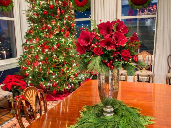 ein Tannenbaum mit Kerzen im Hintergrund, gläserne Vase und Weihnachtsgesteck