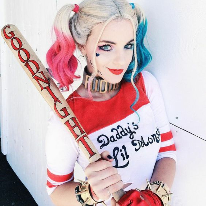 Harley Quinn Suicide Squad blonde Haare mit blauen und pinken Längen weiße Bluse mit roten Streifen Print mit schwarzen Buchstaben zwei Armbänder mit Stacheln Schlagholz