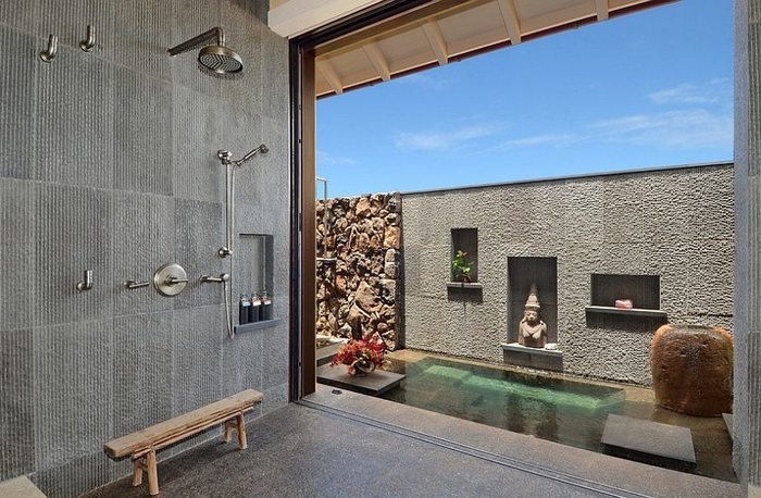 Designer Badezimmer im asiatischen Stil mit Übergang zum Außenbereich, Regendusche montiert an der Wand, Wandnische mit drei Seifenbehälter, Außenbereich mit Buddha-Statue, kleinem Teich und Natursteinwand