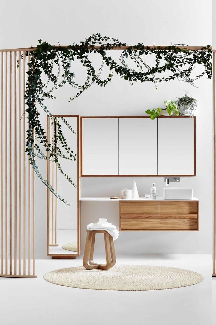 Raumteiler aus Holzgittern mit einem Rankgewächs, runder Teppich in Cremeweiß, Hocker aus Holz, Spiegelschrank mit einer grünen Pflanze darauf