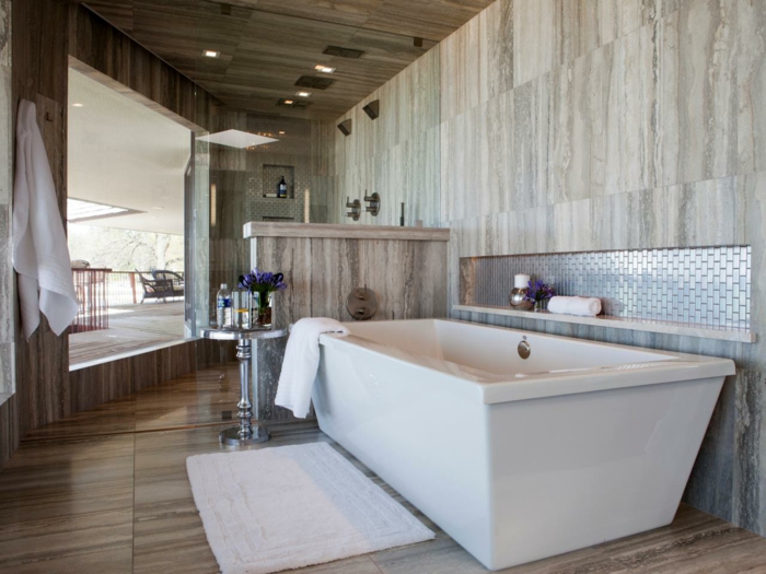 Bad mit Terrassenübergang, Fliesen mit Holzoptik, weiche weiße Fußmatte für Badewanne, Marmor-Trennwand, runder Metalltisch mt Blumendeko