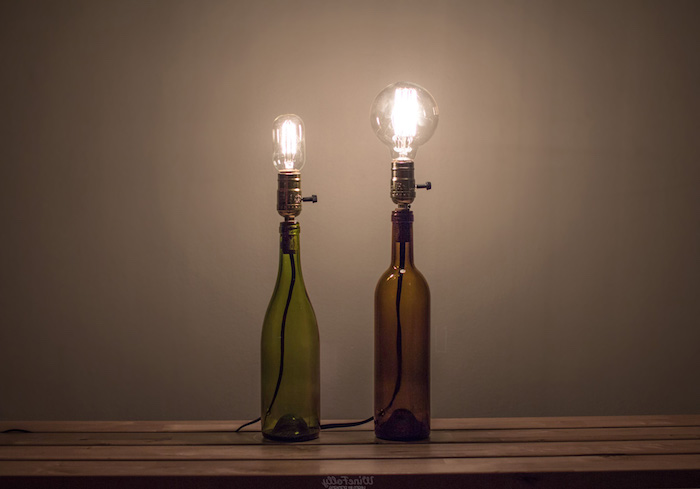 flaschenlampe selber bauen - zwei grüne und braune glasflaschen mit leuchtenden glühbirnen und tisch aus holz