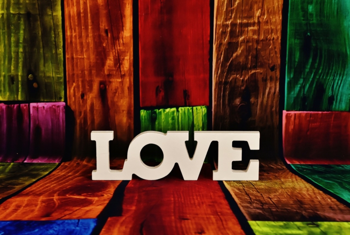 das Wort Liebe mit weißen Buchstaben geschrieben, Bilder zum Valentinstag, buntes Holz als Hintergrund