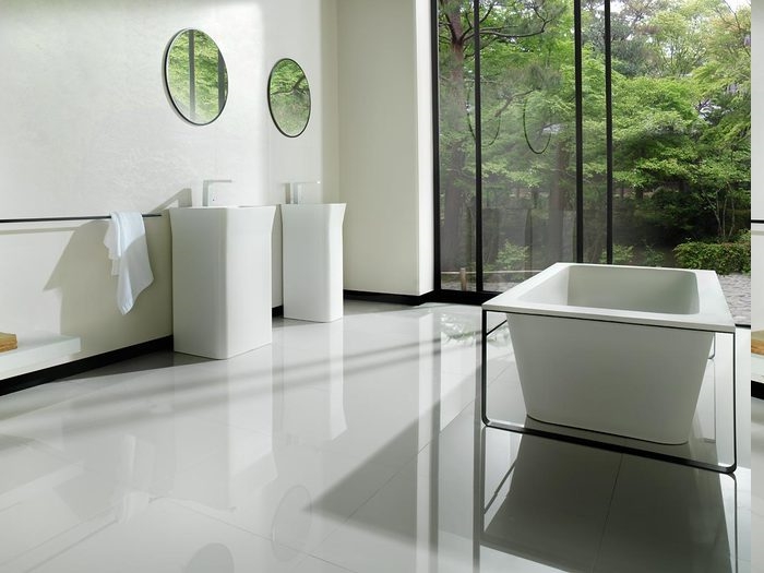 Badeinrichtun im minimalistischen Stil, zwei freistehende Waschbecken aus Keramik mit zwei runden Wandspiegeln darüber, Raumteiler aus Glas, Aussicht zum Wald