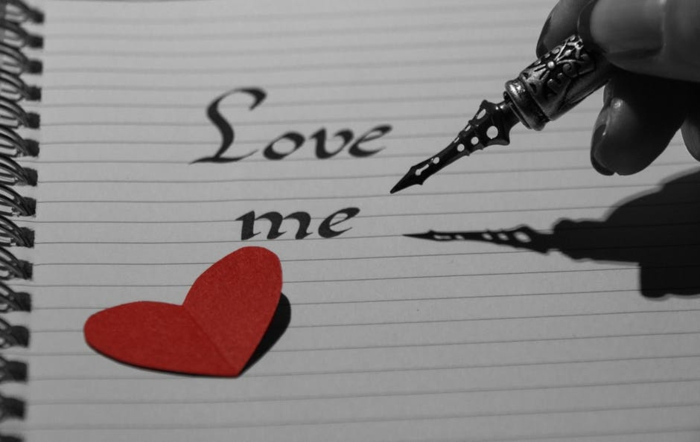 mit einem Füller Liebe mich mit Ornamenten geschrieben - Bilder zum Valentinstag und ein kleines rotes Herzchen aus Papier
