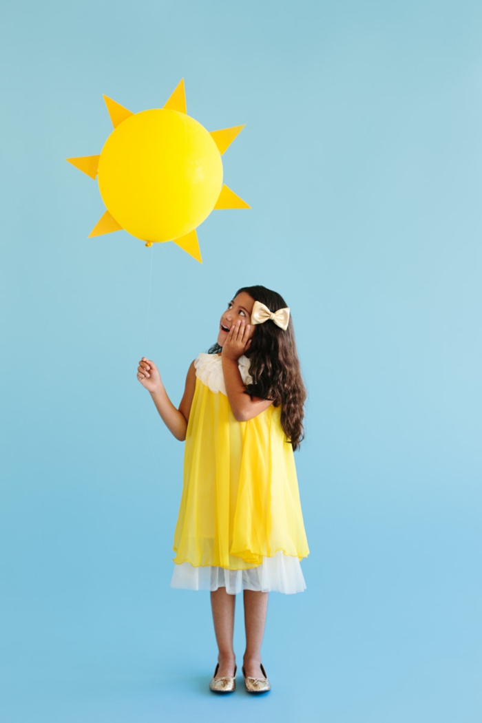 Sonne Kostüm von einem kleinen Mädchen mit gelben Kleid, das Mädchen trägt einen gelben Ballon