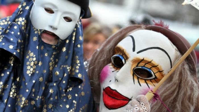 Mann mit blauem Kostüm mit goldenen Sternen und weißer Maske, Frau mit schrecklicher Karnevalmaske