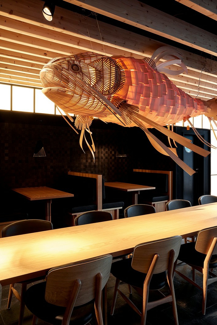 Kronleuchter aus Holz im asiatischen Stil, Lüster in der Form eines Fisches in einem asiatischen Restaurant mit Tischen aus Massivholz und Holzstühlen mit Ledersitzen