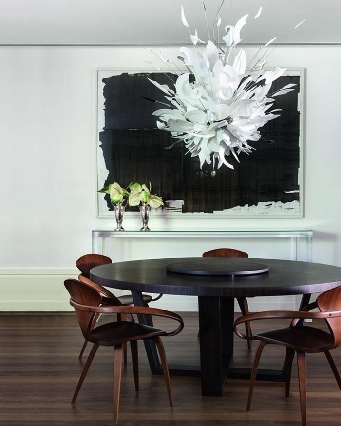 weißer Kronleuchter aus zerbrochenem Geschirr aus weißem Porzellan, schwarzer Esstisch in runder Form, braune Holzstühle mit minimalistischem Design