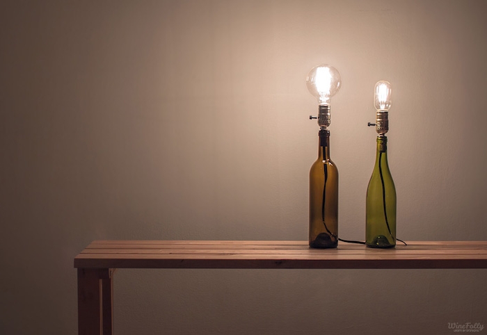 eine bank aus holz und zwei lampen aus grünen und braaunen glasflaschen und mit glühbirnen