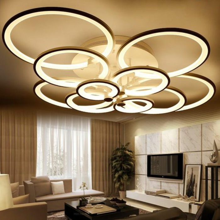 LED-Leuchte mit vielen Ringen aus Metall, Wohnzimmer beige gestalten - beige Couch mit vielen Couchkissen, lange Gardinen in Beige
