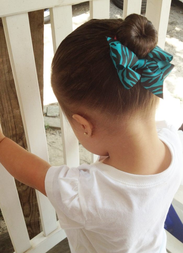 ein kleines Mädchen mit einer Hochsteckfrisur und einer blauen Schleife