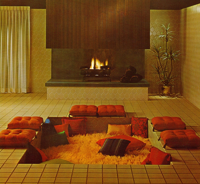 japanische Sitzecke mit simpler Gestaltung - nieder liegende Relaxecke mit orangen Kissen und gelbem Teppich, Wohnzimmer mit offenem Kamit, offene Feuerstelle mit einer Pflanze rechts davon