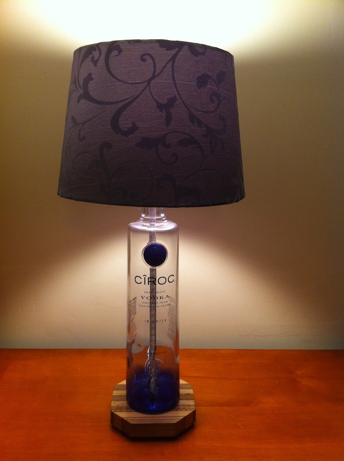 eine violette schlafzimmer lampe aus einer durchsichtigen weißen glasflasche und ein tisch aus holz