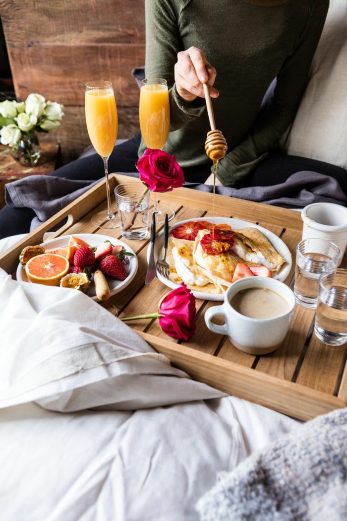Frühstück im Bett zum Valentinstag, Pfannkuchen mit Honig und Früchten, Orangensaft und Cappuccino, rote Rosen