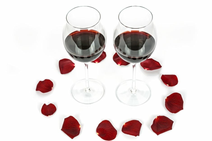 ein Bild mit schönen Valentinstagsgrüße - zwei Tasse roter Wein von Rosenblütten umgeben