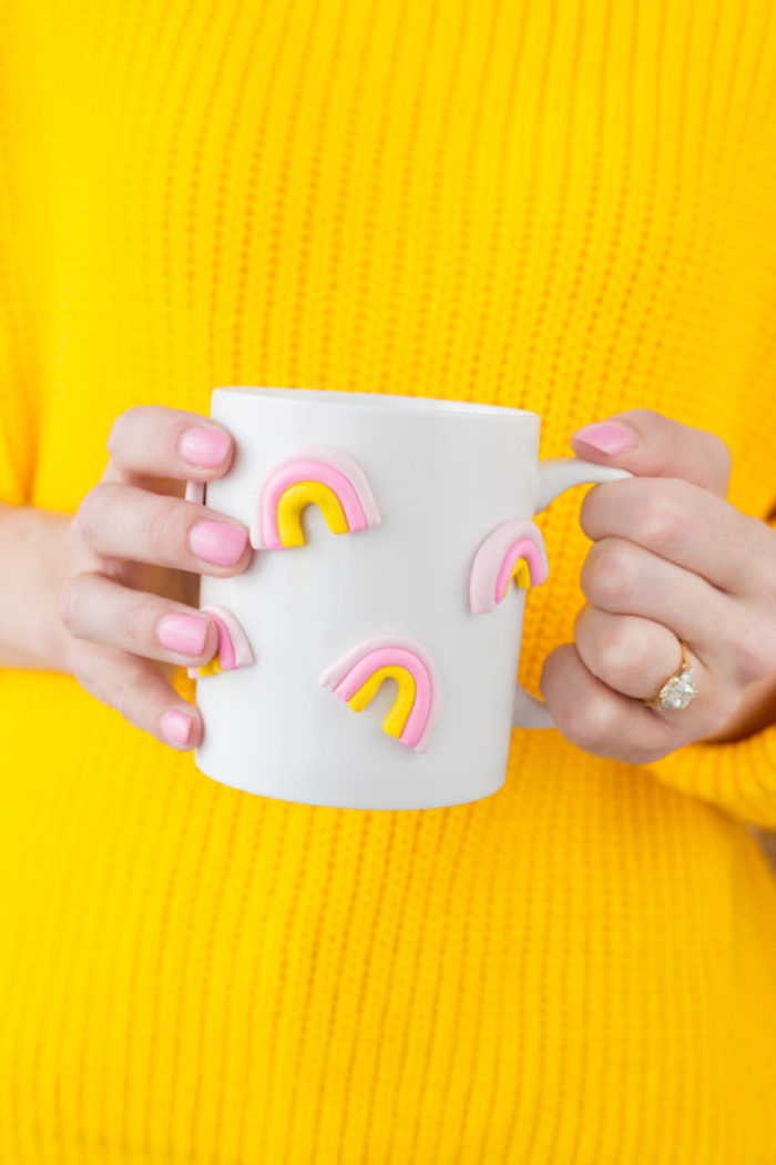 3D Tasse mit kleinen Regenbogen, gelber Pullover, goldener Ring mit Kristallstein, rosafarbener Nagellack