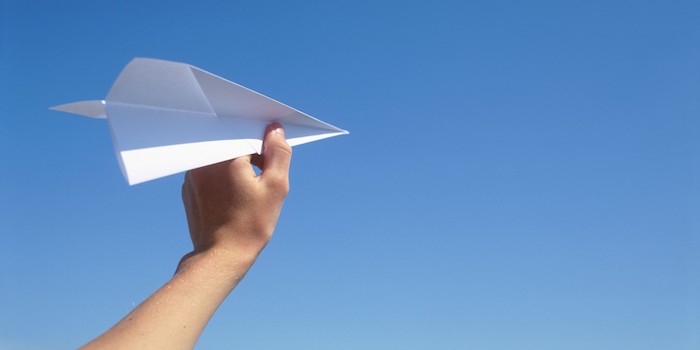 bastelideen mit papier, ein blauer himmel und eine hand mit einem großen weißen papierflieger, einen papierflieger basteln