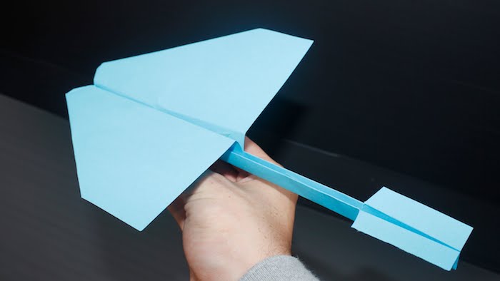 ein grauer tisch, einen papierflieger basteln, eine hand mit einem großen blauen papierflieger schwalbe