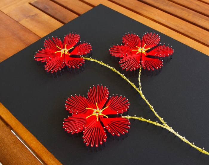 drei Blumen in roter Farbe, Blumen Fadenbilder auf einem schwarz gestrichenen brett