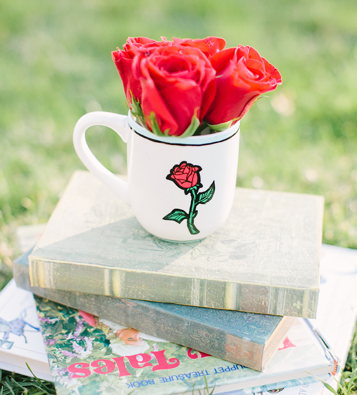 Weiße Tasse mit der Rose aus "Die Schöne und das Biest", kleiner Rosenstrauß und einige Bücher