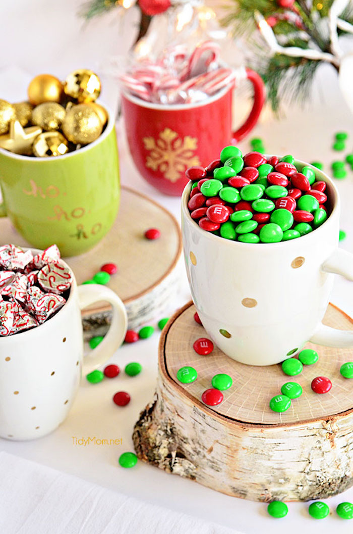 Schöne Geschenkidee zu Weihnachten, selbst bemalte Tassen voll mit Bonbons, Zuckerstangen und Weihnachtskugeln