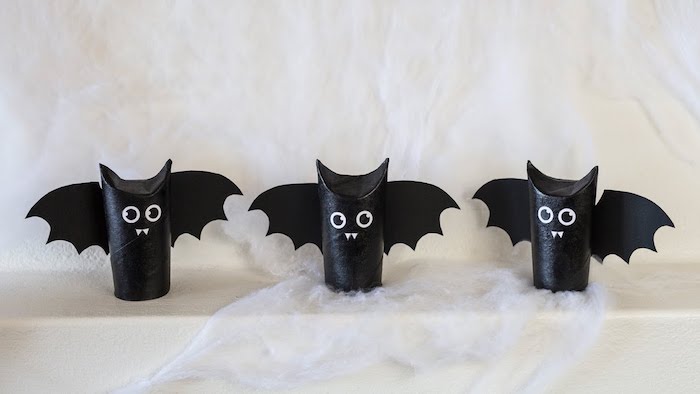 dekoration mit drei kleinen schwarzen fledermäusen mit schwarzen augen, weißen zähnen und schwarzen flügeln aus papier, fledermaus basteln aus klorollen