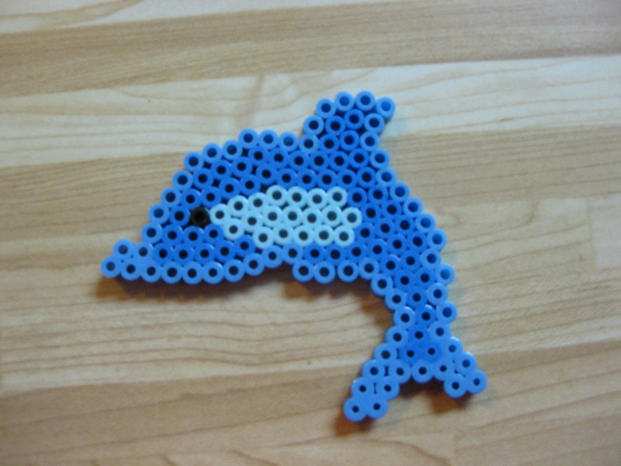 kleine Figur aus Steckperlen, ein winziges blaues Delfin mit schwarzen Perlenauge