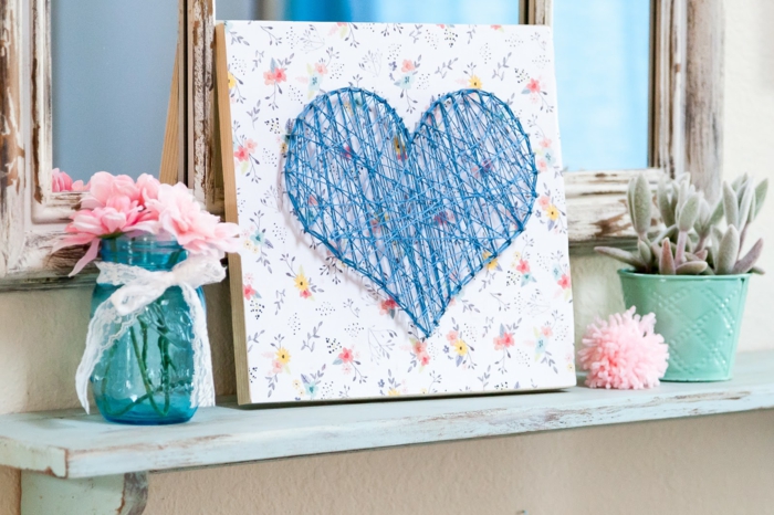 Nagelbilder mit blauen Fäden, Herzform an einerschönen Tafel mit Blumenmuster versehen