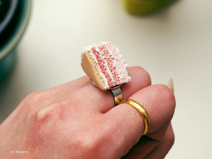 eine hand mit einem goldenen ring mit einer kleinen selbstgebastelten pinken torte aus einer fimo knete