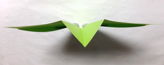 ein grüner kleiner papierflieger, ein weißer tisch, einen grünen papierflieger basteln