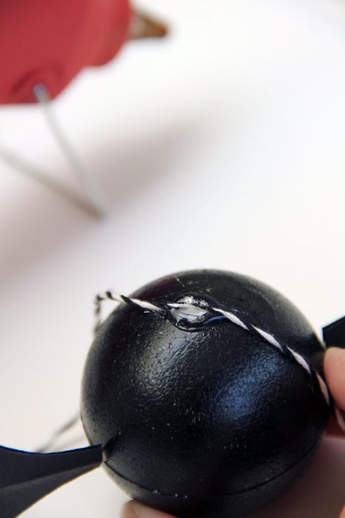 ein weißer tisch und ein schwarzer ball, eine hand und eine diy fledermaus mit schwarzen flügeln aus papier
