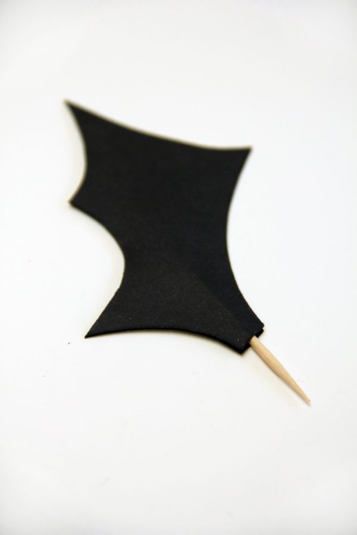 ein weißer tisch, ein kleiner zahnstocher mit einem schwarzen fledermaus flügel aus papier
