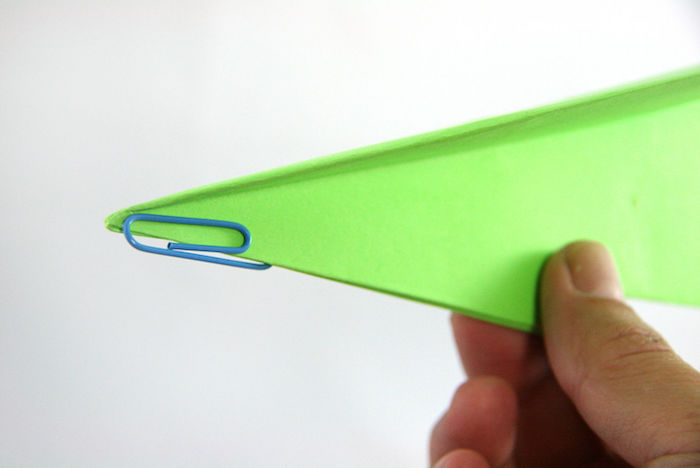 einen papierflieger selber bauen, ein bild mit einer hand mit einem kleinen grünen papierflieger, bastelideen mit papier