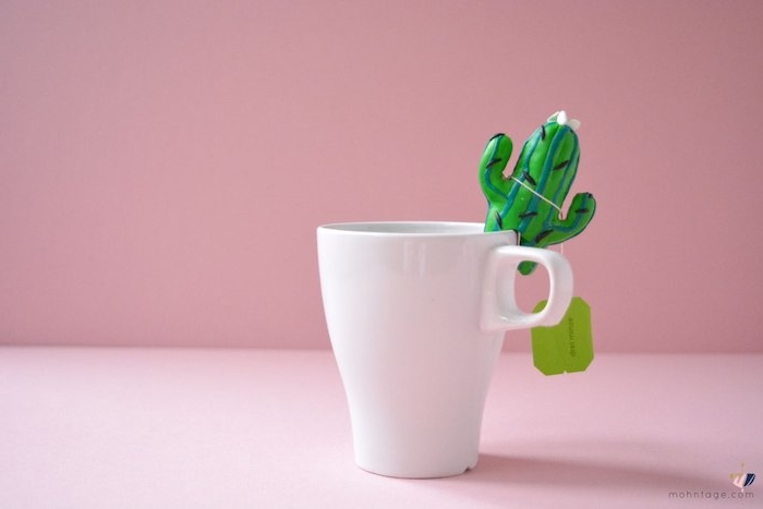 eine tasse mit tee und einem selbstgebastelten grünen kaktus aus einer grünen fimo knete und eine pinke wand