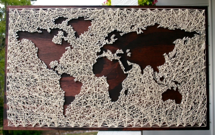 eine braune Tafel mit einer Weltkarte, Schattenbilder von den Kontinenten, weiße Fäden, Fadenkunst
